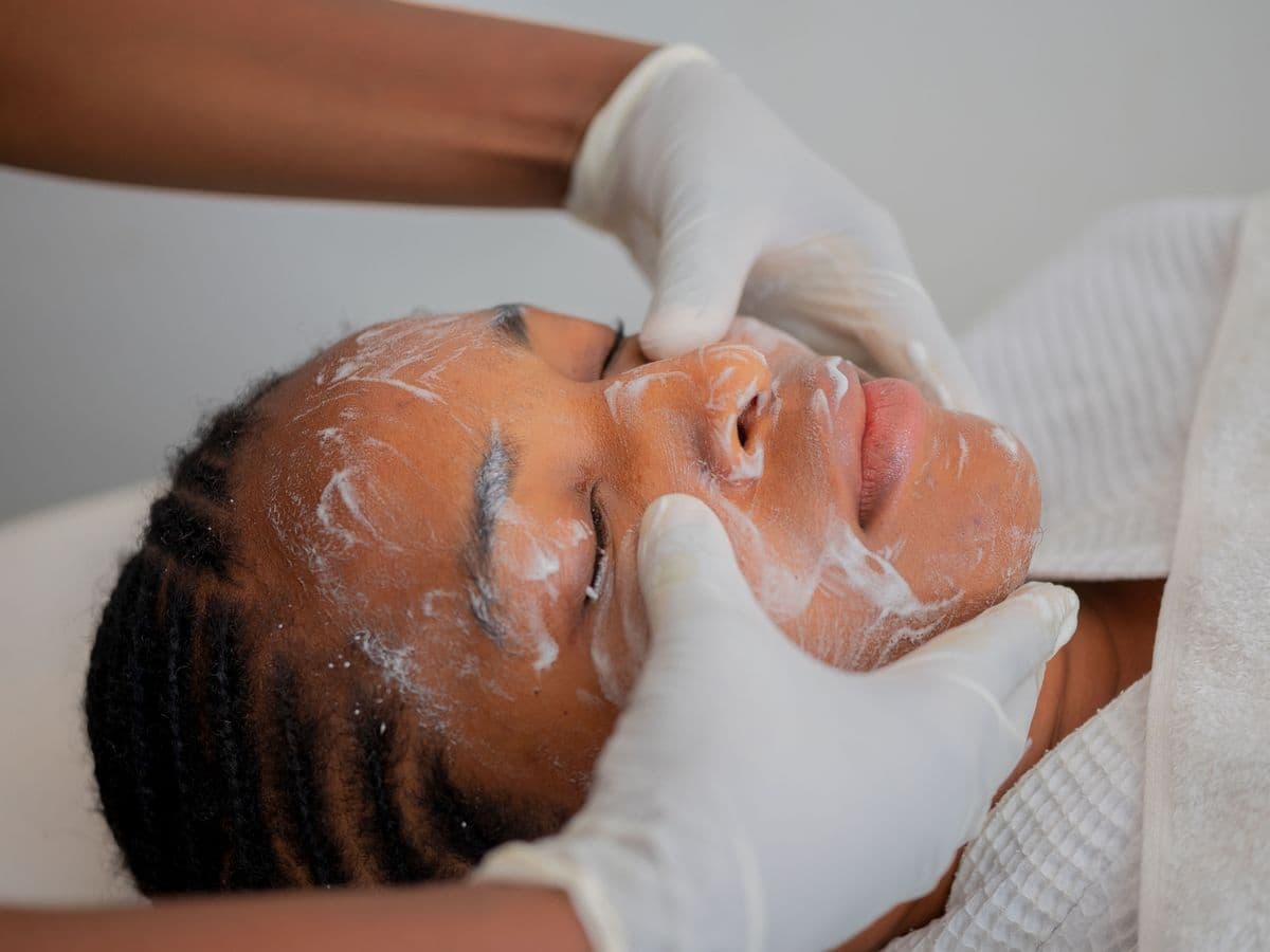 Une praticienne applique un soin sur le visage d'une cliente allongée en cabine.